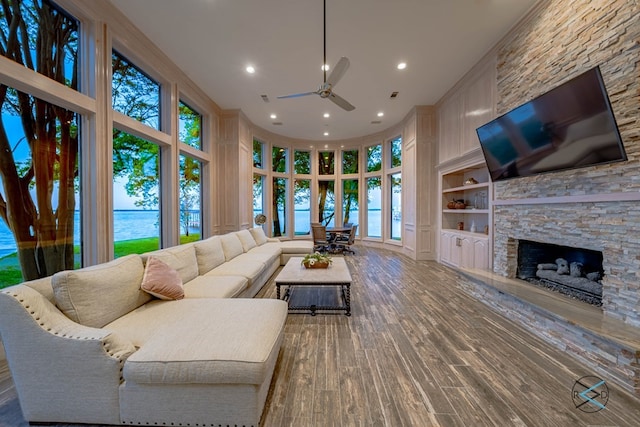 living room with a healthy amount of sunlight, built in shelves, a stone fireplace, and wood-type flooring