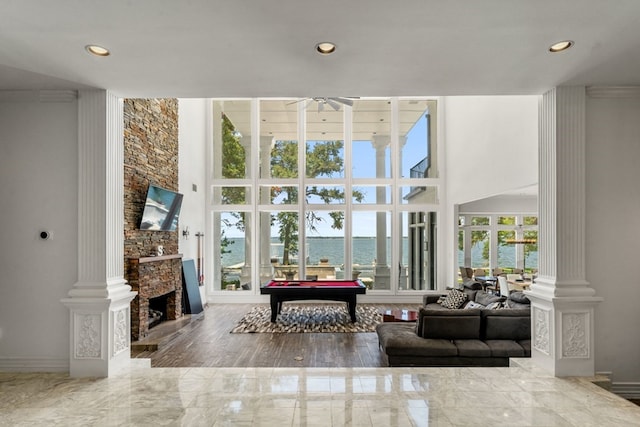 living room featuring ceiling fan, a stone fireplace, hardwood / wood-style flooring, ornate columns, and pool table