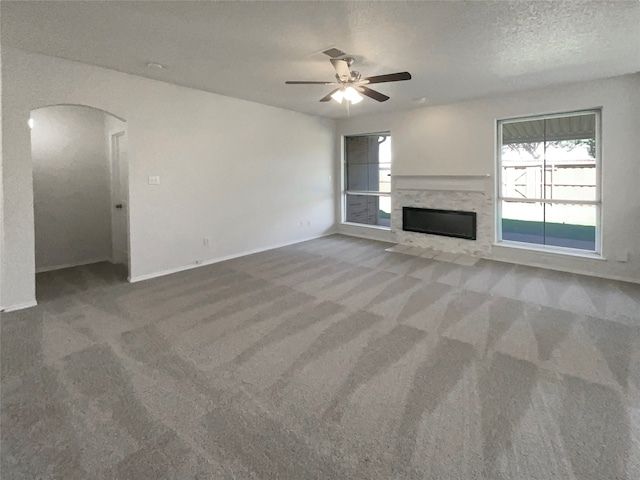 unfurnished living room with ceiling fan, a textured ceiling, a premium fireplace, and carpet