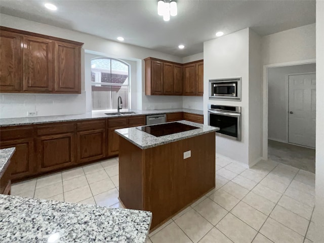 kitchen with light stone counters, light tile patterned floors, sink, stainless steel appliances, and a center island