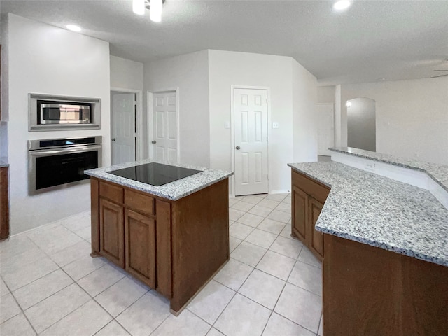 kitchen with light stone counters, a center island with sink, appliances with stainless steel finishes, and a textured ceiling