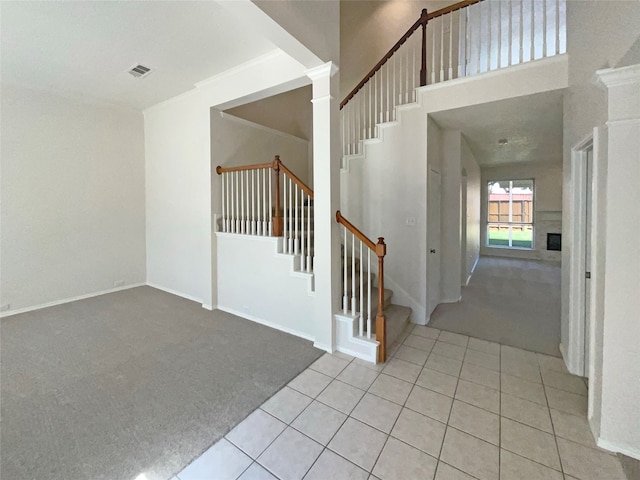 foyer entrance featuring light colored carpet, ornamental molding, and a high ceiling