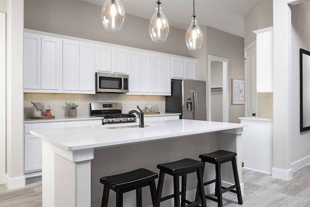 kitchen with stainless steel appliances, white cabinetry, and a center island with sink