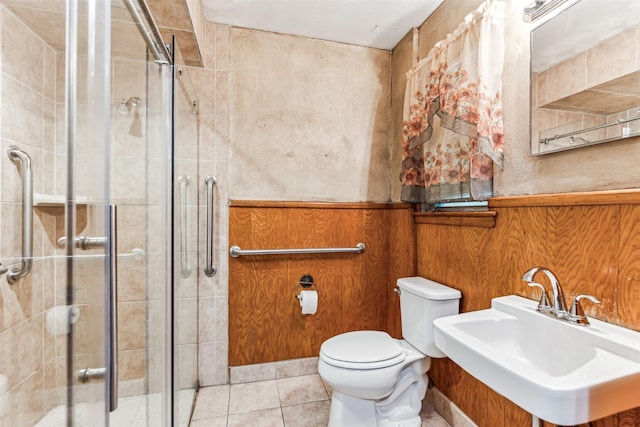 bathroom with walk in shower, sink, tile patterned flooring, toilet, and wood walls