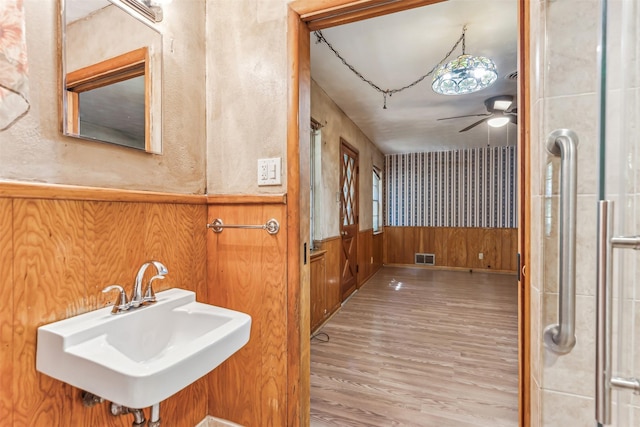 bathroom featuring wood-type flooring, ceiling fan, wooden walls, and sink