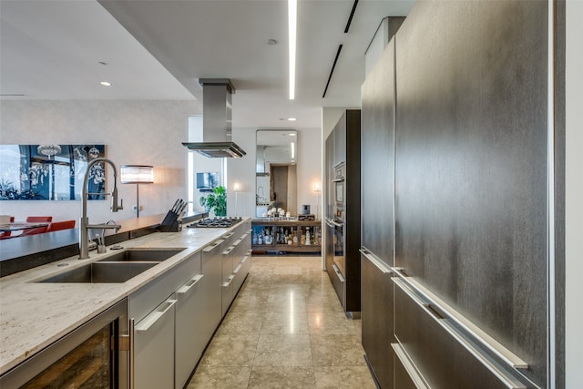 kitchen featuring appliances with stainless steel finishes, light stone counters, island exhaust hood, beverage cooler, and sink