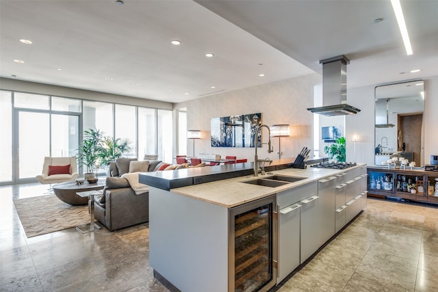 kitchen featuring sink, a kitchen island with sink, island range hood, light stone countertops, and beverage cooler