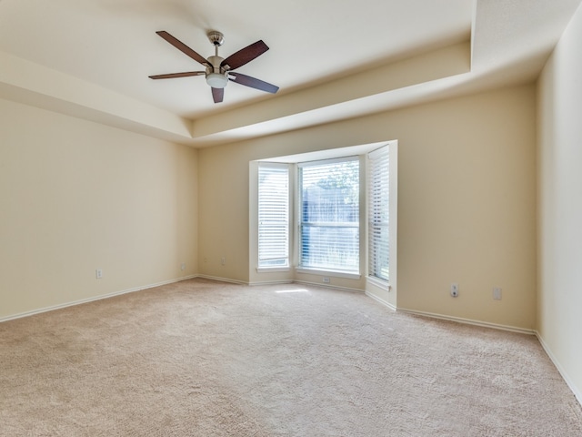 carpeted spare room with ceiling fan and a tray ceiling