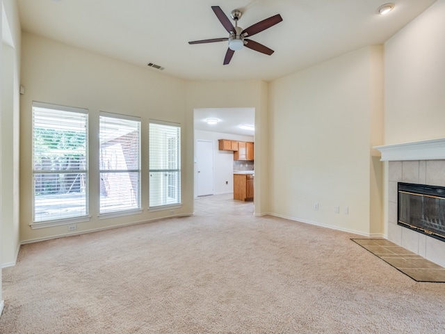 unfurnished living room with light carpet, a tiled fireplace, and ceiling fan