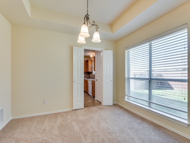 carpeted spare room featuring a raised ceiling and a notable chandelier