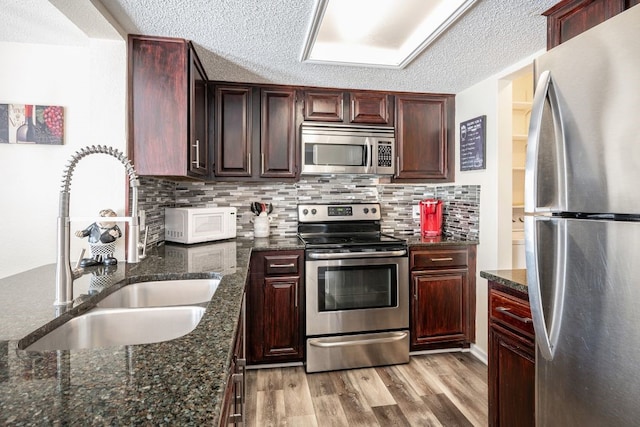 kitchen with light hardwood / wood-style floors, a textured ceiling, appliances with stainless steel finishes, and sink