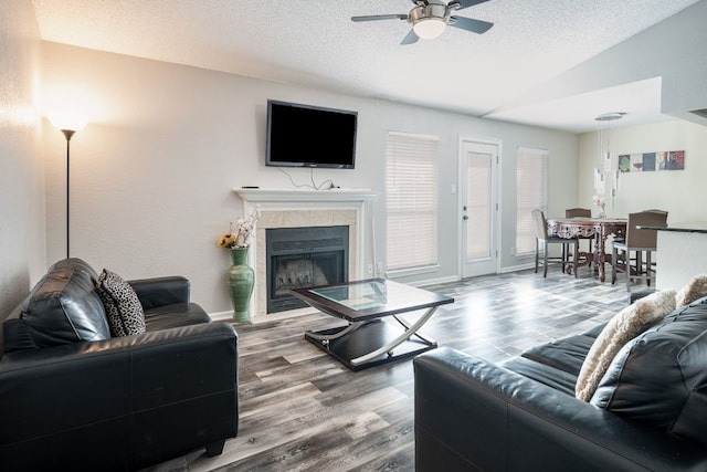 living room with a textured ceiling, a tiled fireplace, ceiling fan, and hardwood / wood-style flooring