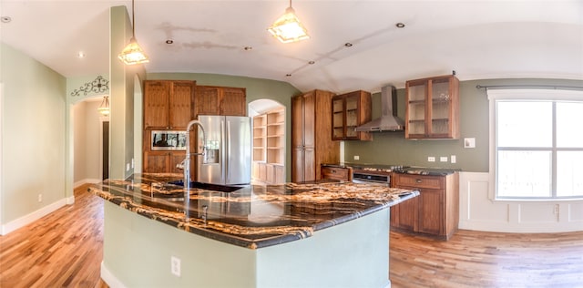 kitchen featuring wall chimney exhaust hood, light wood-type flooring, pendant lighting, vaulted ceiling, and stainless steel appliances