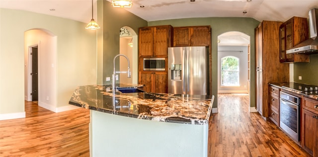 kitchen featuring an island with sink, lofted ceiling, hanging light fixtures, stainless steel appliances, and hardwood / wood-style floors