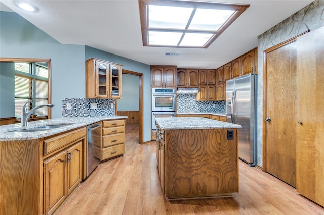 kitchen featuring kitchen peninsula, appliances with stainless steel finishes, light stone countertops, sink, and light hardwood / wood-style floors