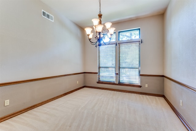 carpeted spare room featuring an inviting chandelier