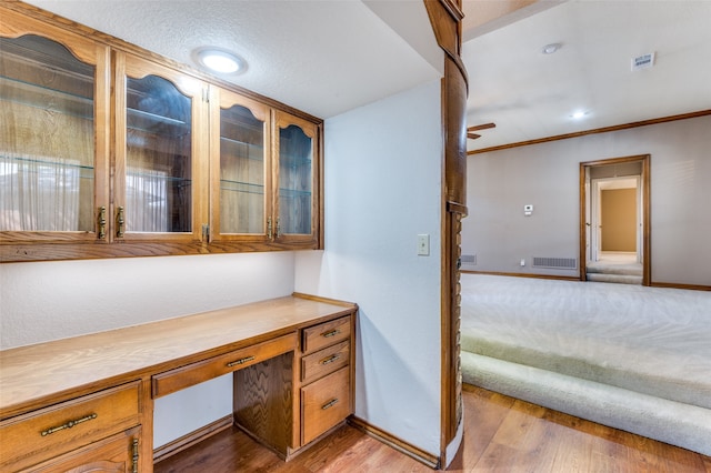 unfurnished office featuring ceiling fan, light hardwood / wood-style floors, built in desk, and crown molding