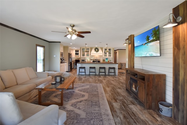 living room with dark hardwood / wood-style floors, sink, wooden walls, ornamental molding, and ceiling fan