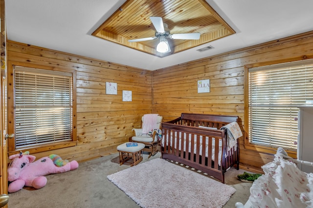 carpeted bedroom featuring a ceiling fan, a nursery area, visible vents, and wood walls