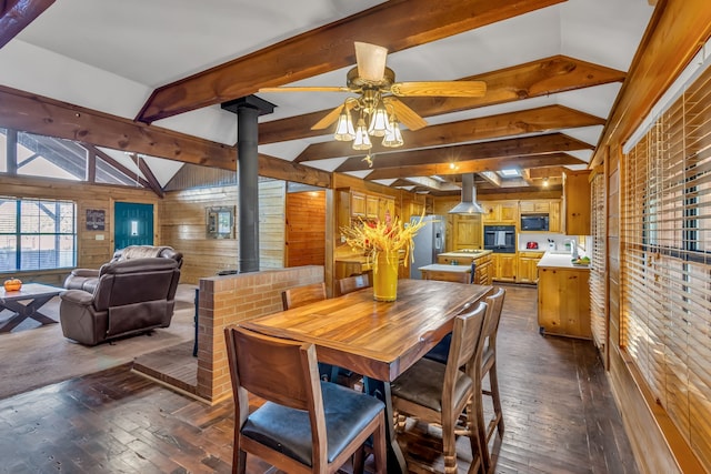 dining space with wooden walls, vaulted ceiling with beams, a wood stove, and ceiling fan