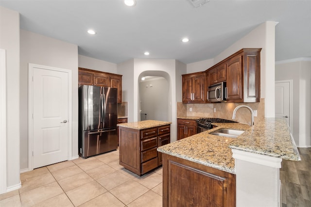 kitchen featuring light stone countertops, sink, stainless steel appliances, backsplash, and a kitchen island