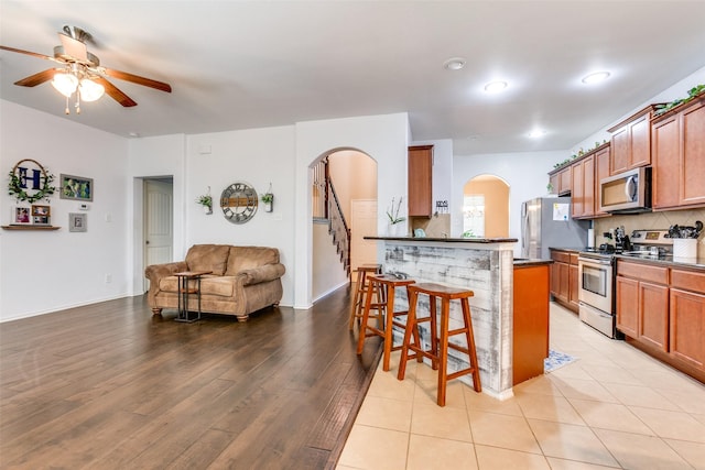 kitchen with ceiling fan, a kitchen breakfast bar, light hardwood / wood-style floors, decorative backsplash, and appliances with stainless steel finishes