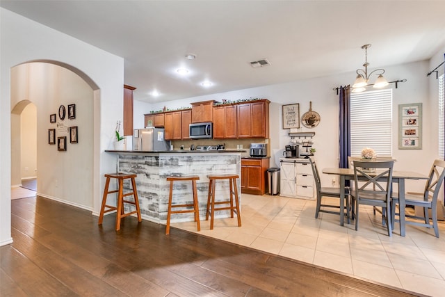 kitchen with hanging light fixtures, stainless steel appliances, kitchen peninsula, a chandelier, and light hardwood / wood-style floors