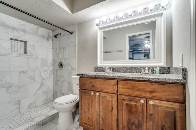 bathroom with vanity, toilet, a textured ceiling, and tiled shower