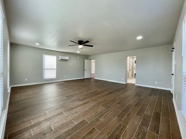 unfurnished living room featuring a textured ceiling, dark hardwood / wood-style floors, an AC wall unit, and ceiling fan