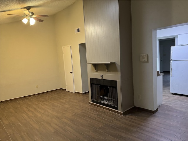 unfurnished living room with ceiling fan, a textured ceiling, a multi sided fireplace, and dark hardwood / wood-style flooring