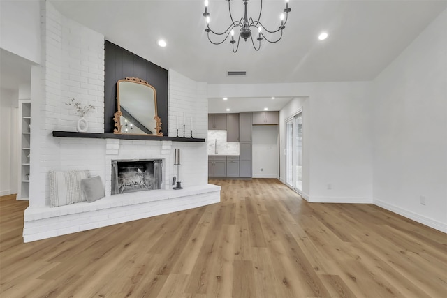 unfurnished living room with a fireplace, sink, light hardwood / wood-style flooring, and a notable chandelier