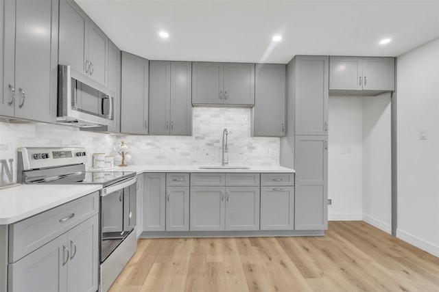 kitchen featuring gray cabinets, light wood-type flooring, appliances with stainless steel finishes, and sink