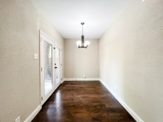 unfurnished dining area featuring french doors, an inviting chandelier, dark wood-type flooring, and a wealth of natural light