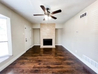 unfurnished living room with ceiling fan, a fireplace, and dark hardwood / wood-style flooring