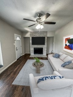 living room featuring ceiling fan, a fireplace, dark wood-type flooring, and a textured ceiling