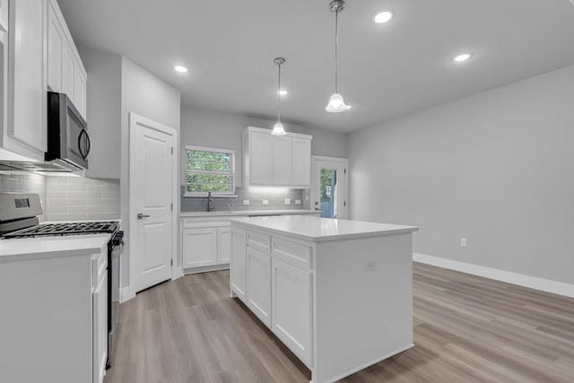 kitchen with a kitchen island, stainless steel gas range oven, white cabinetry, and light hardwood / wood-style flooring