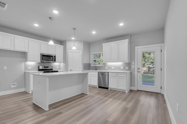 kitchen with light hardwood / wood-style flooring, stainless steel appliances, white cabinetry, and hanging light fixtures