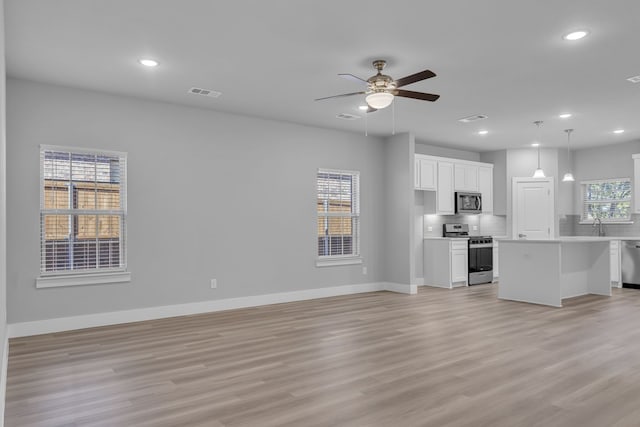 unfurnished living room with light hardwood / wood-style floors, ceiling fan, and sink