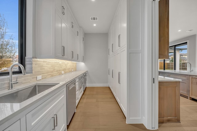 kitchen featuring stainless steel dishwasher, white cabinets, sink, and light hardwood / wood-style flooring