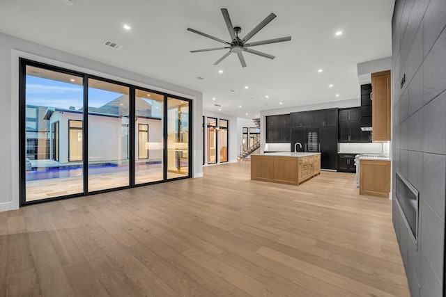 kitchen featuring light hardwood / wood-style flooring, sink, black fridge, ceiling fan, and a center island with sink