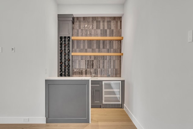 bar featuring gray cabinetry, beverage cooler, and light hardwood / wood-style flooring