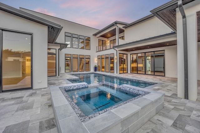 pool at dusk with an in ground hot tub and a patio