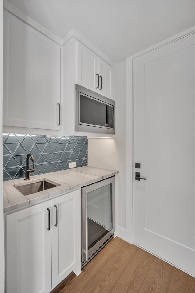 kitchen featuring stainless steel microwave, wine cooler, sink, light hardwood / wood-style flooring, and white cabinets