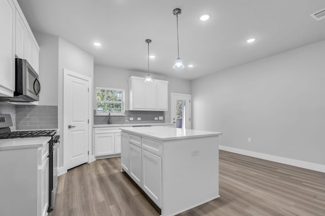 kitchen with pendant lighting, white cabinetry, a kitchen island, stainless steel appliances, and hardwood / wood-style floors