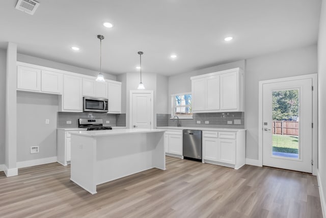 kitchen with appliances with stainless steel finishes, white cabinetry, a kitchen island, pendant lighting, and light wood-type flooring