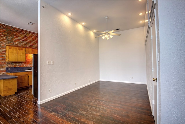 unfurnished living room with ceiling fan, dark wood-type flooring, and brick wall