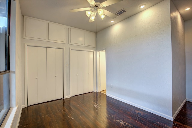 unfurnished bedroom featuring ceiling fan, two closets, and dark wood-type flooring