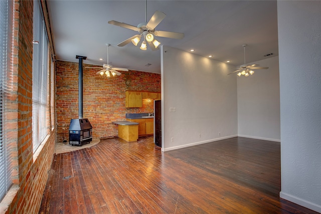 unfurnished living room featuring dark hardwood / wood-style flooring, ceiling fan, a wood stove, and brick wall