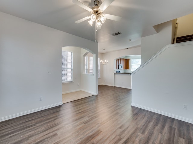 unfurnished living room with ceiling fan with notable chandelier and dark hardwood / wood-style flooring