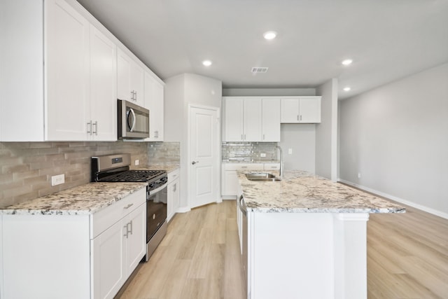 kitchen featuring an island with sink, sink, white cabinetry, stainless steel appliances, and light hardwood / wood-style floors